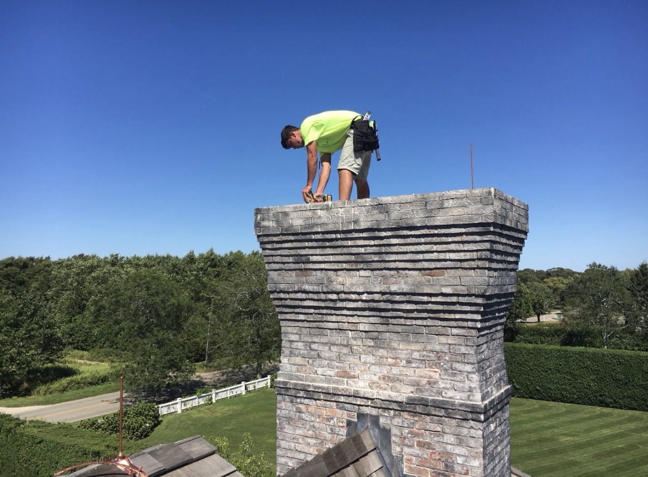 WB Lightning Rods crew member installing a copper lightning rod on top of a large stone chimney at an estate home